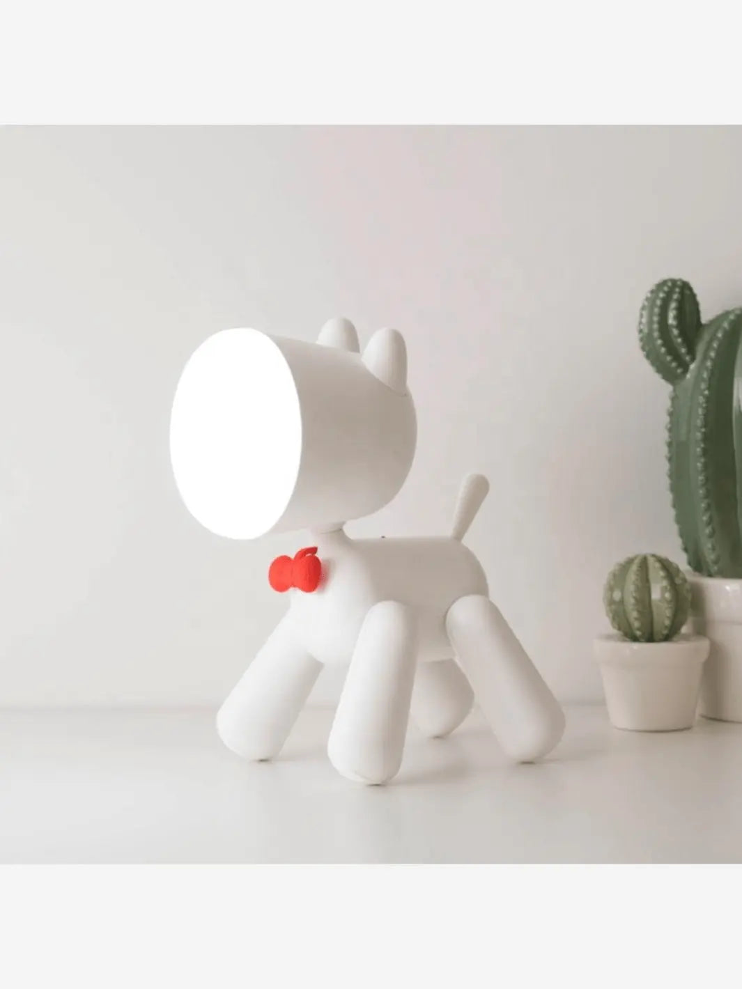 lampe de chevet pour enfant en forme de chien mignon qui porte un noeud papillon posee sur une table de chevet avec des cactus