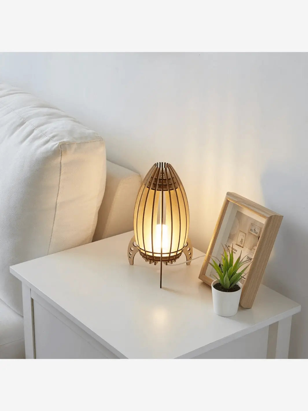 lampe de chevet en bois pour enfant en forme de fusee prete a decoller allumee et posee sur une table de chevet blanche