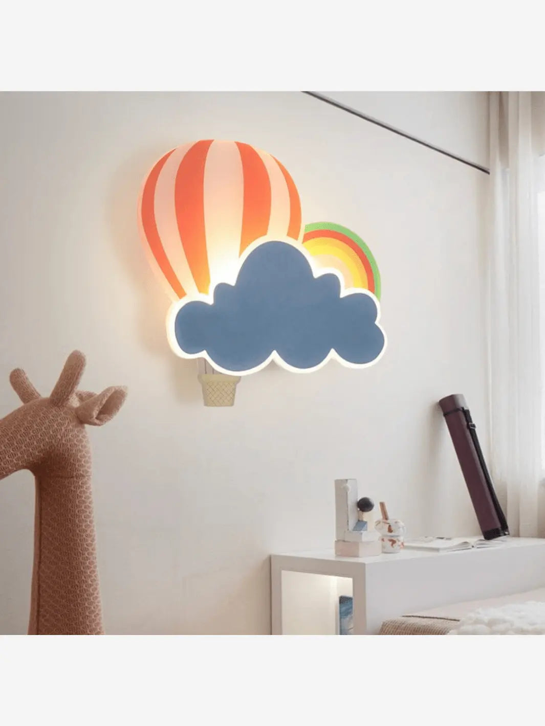Lampe de chevet murale pour enfant qui représente un nuage, un arc-en-ciel ainsi qu'une montgolfière au dessus d'une table de chevet