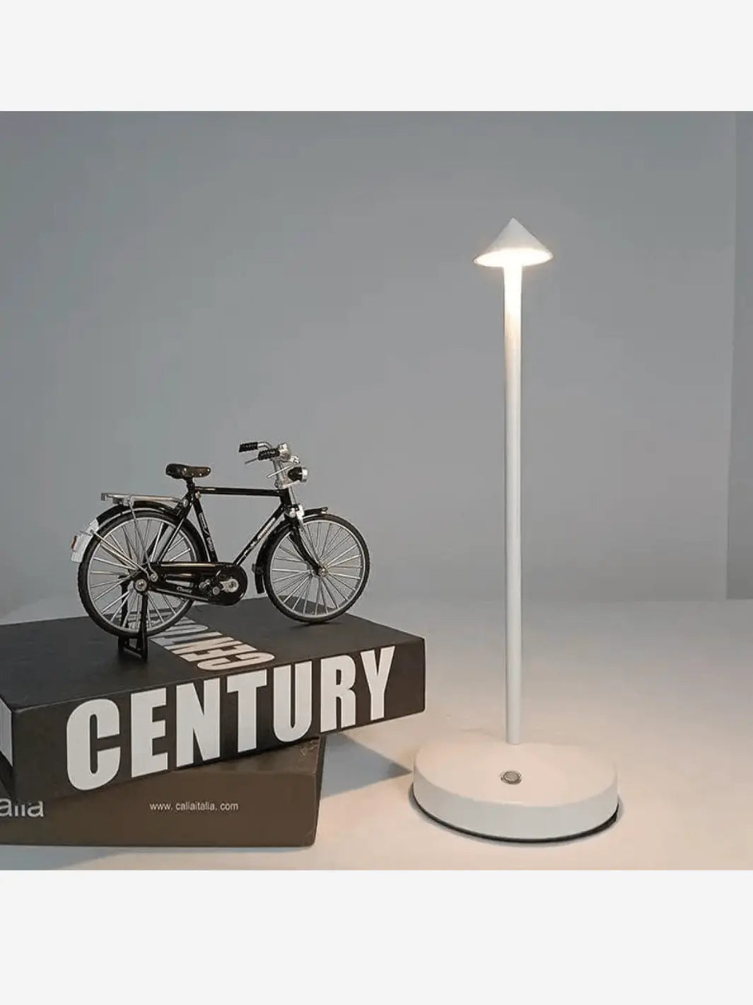 lampe de chevet rechargeable portable sans fil minimaliste pratique blanche posee sur une table a cote de livres de decoration et de mini velos de decoration