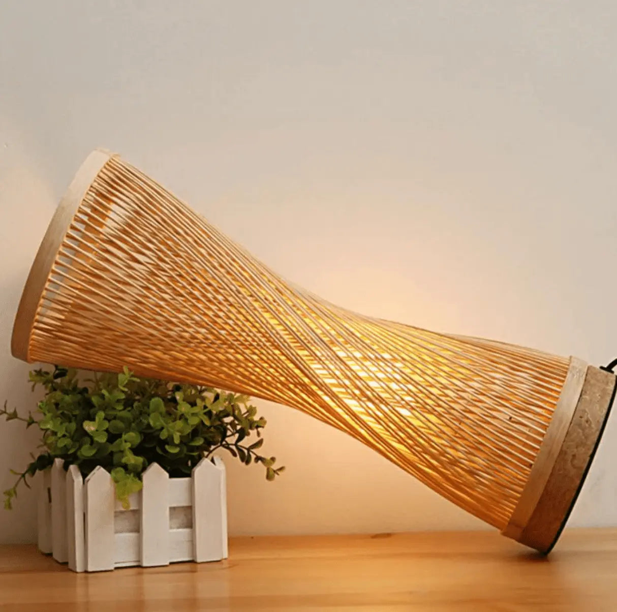 Une lampe de chevet en bambou qui se trouve sur un table de chevet en bois
