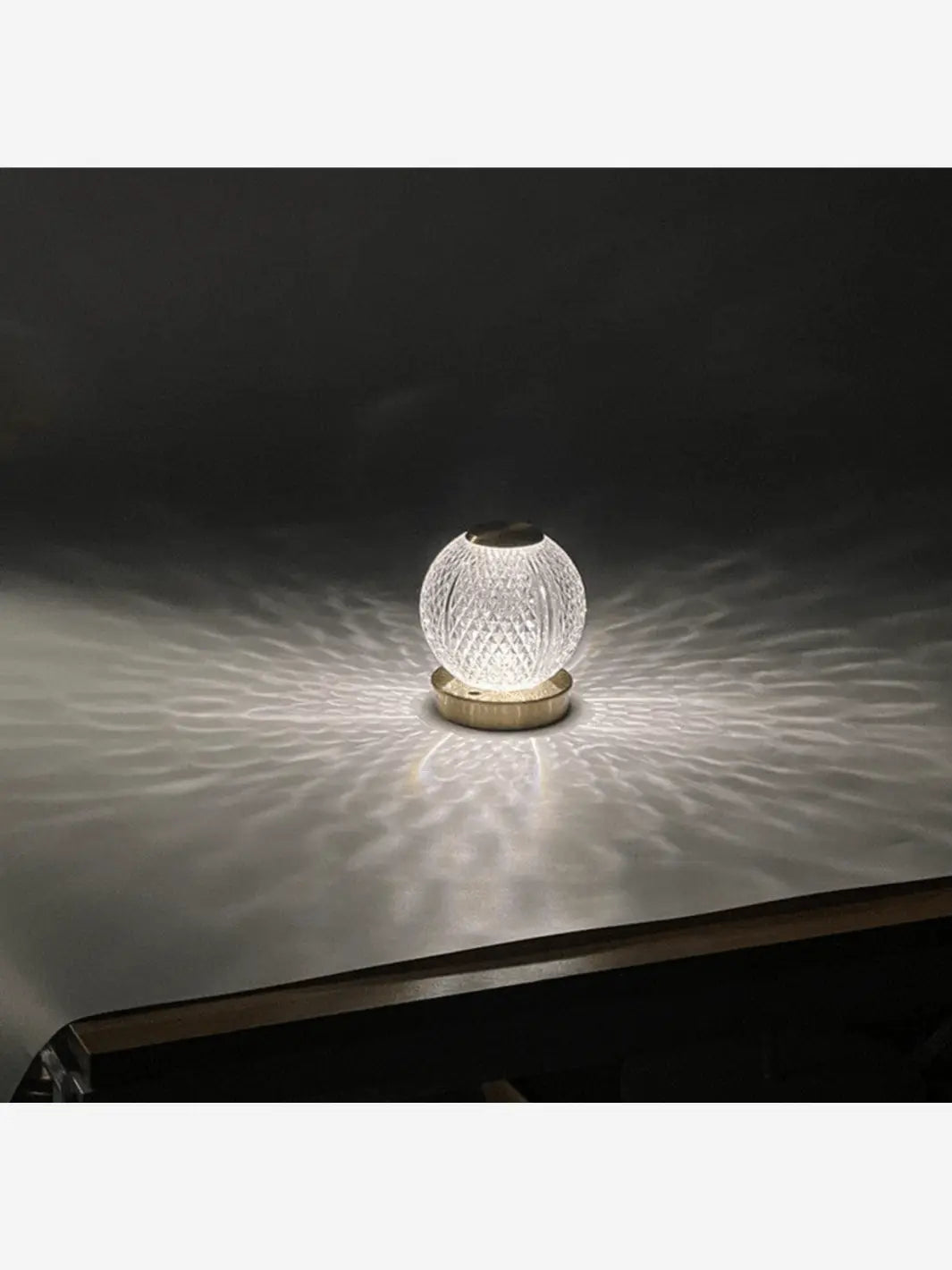 lampe de chevet representant une boule en cristal allumee brillante posee sur un socle couleur or