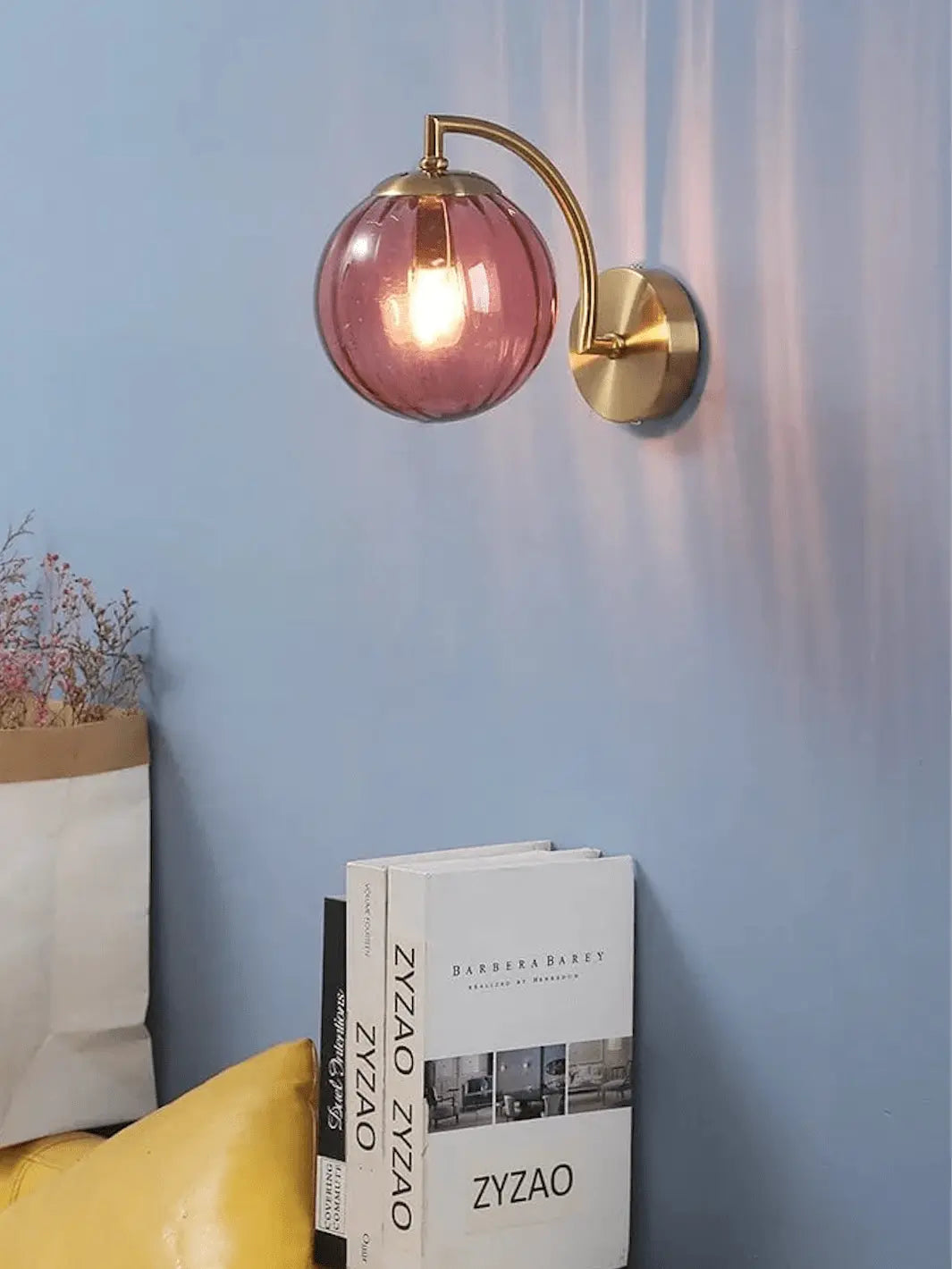 lampe de chevet murale moderne et design avec socle couleur or et bulle lumineuse rose poudree sur un mur avec deco autour